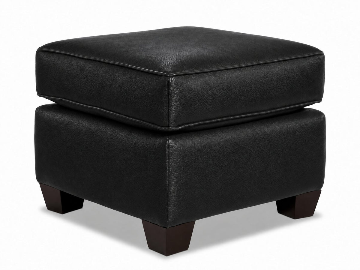 City Leather Ottoman - Black in a three-quarter view with a thick piped cushion, leather upholstery and dark wood legs
