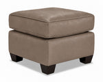 City Leather Ottoman - Stone in a three-quarter view with a thick piped cushion, leather upholstery and dark wood legs