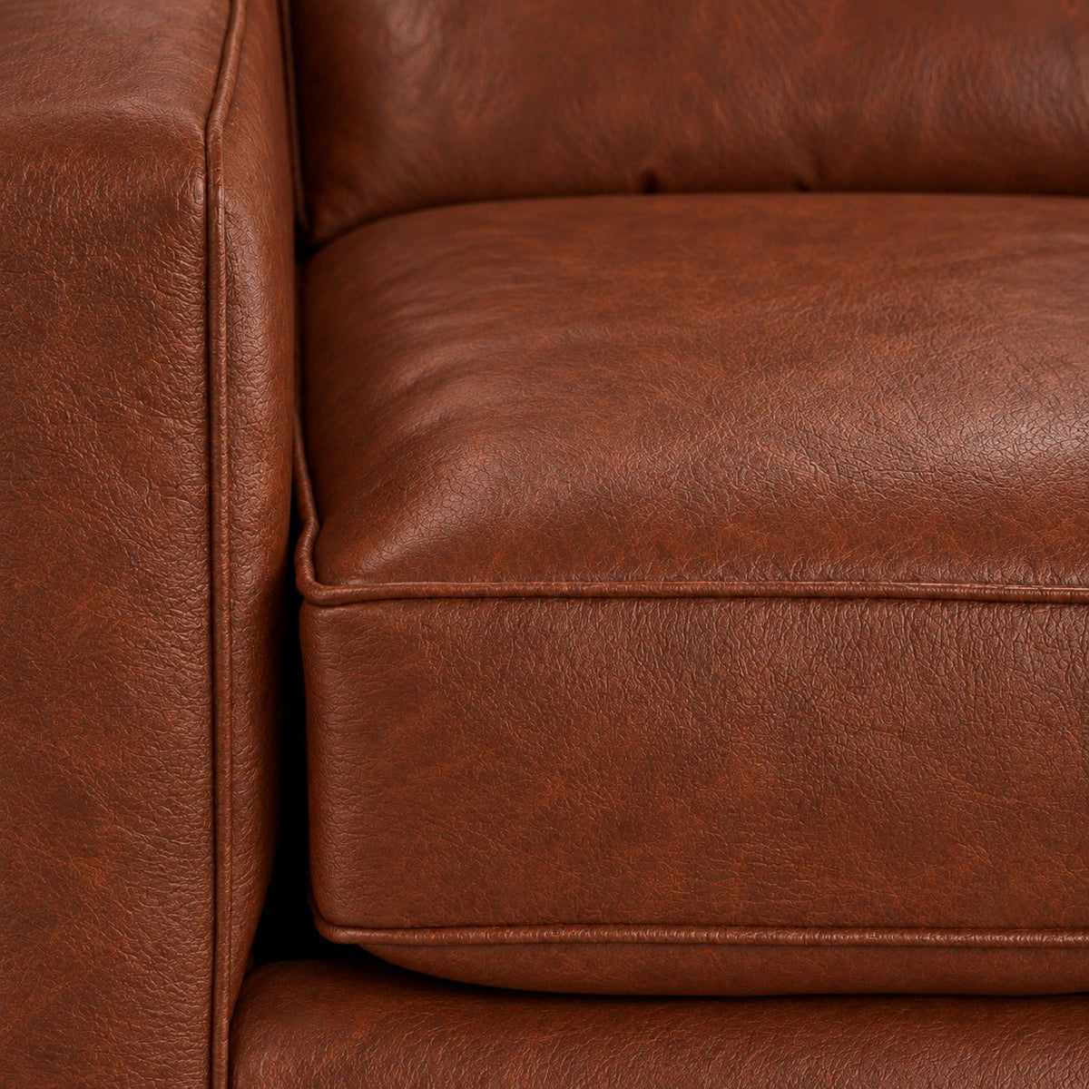 Close-up of the City Leather Loveseat - Brown showing the leather grain, piped seat cushion and matching upholstered arm