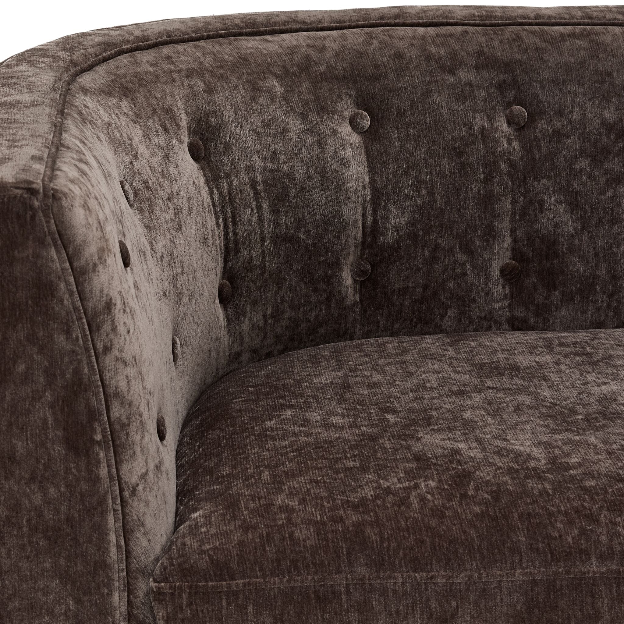 Tresor chair close-up showing dark brown velvet-finish upholstery, curved arm and button-tufted back