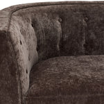 Tresor sofa close-up showing dark brown polyester upholstery, curved arm and button-tufted back